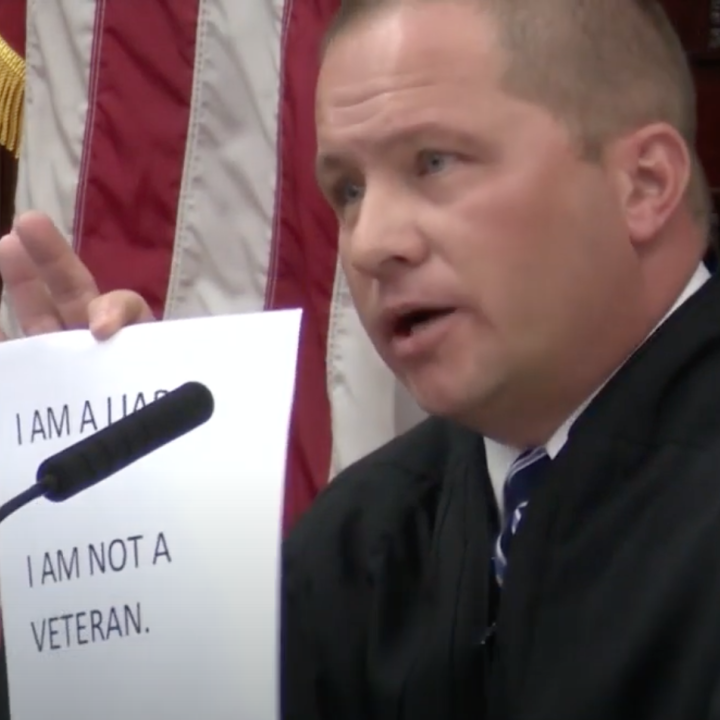 Image of Judge Pinski holding up sign reading I am a liar, I am not a veteran
